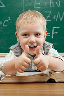 young boy gives a thumbs up from his desk