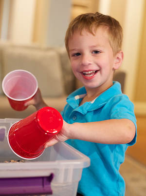 Boy using two plastic cups while playing in a bucket of dry beans.