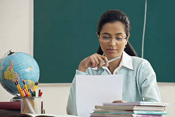 teacher at desk reading a paper