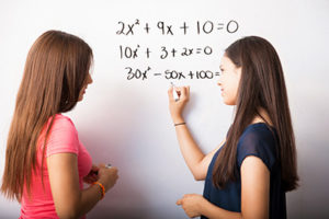 Two girls solving math problem on whiteboard