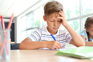 Boy resting his head on hand while working on assignment