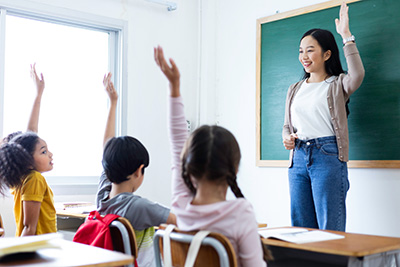 teacher smiles at students with raised hands