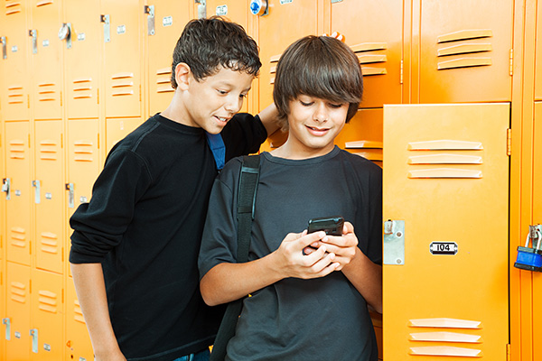 Two boys by a locker looking at cell phone